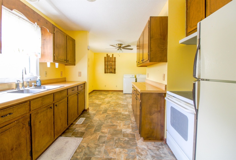 Kitchen featuring white appliances, wood finish cabinets, stone finish flooring, and light countertops