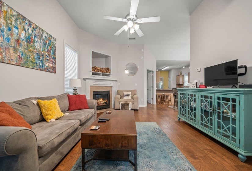 Living room with a tile fireplace, dark wood-style floors, a ceiling fan, and a high ceiling