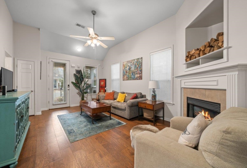 Living room featuring a fireplace, dark wood-type flooring, a ceiling fan, and vaulted ceiling
