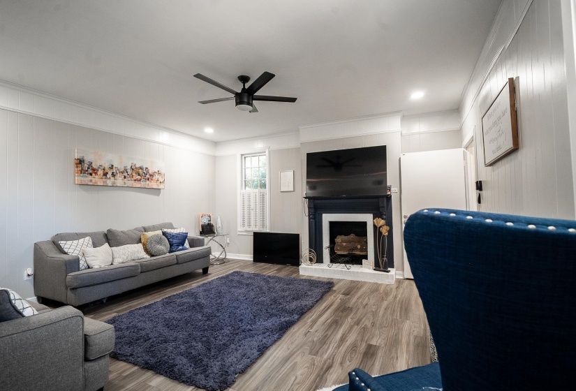 Living area featuring a ceiling fan, wood finished floors, a fireplace with raised hearth, crown molding, and recessed lighting
