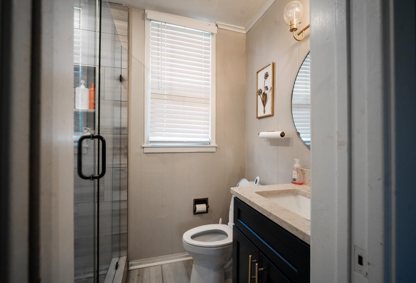 Bathroom featuring a shower stall, vanity, a baseboard radiator, wooden walls, and light wood-style floors