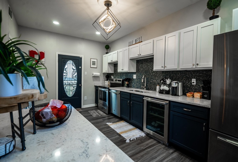 Dual tone kitchen with dual tone cabinets, wine cooler, stainless steel appliances, dark wood finished floors, and light stone counters
