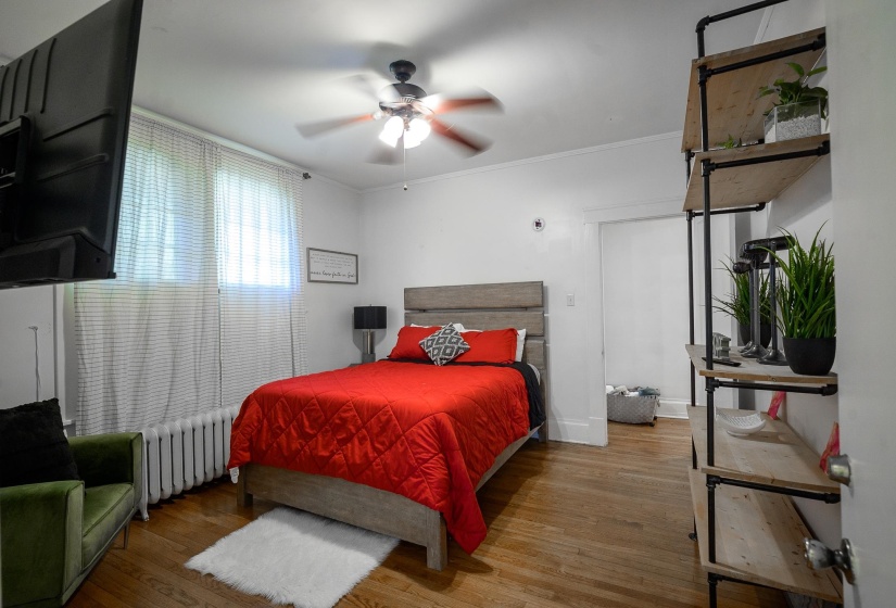Bedroom with wood finished floors, radiator heating unit, ornamental molding, and a ceiling fan