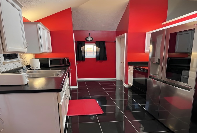 Kitchen featuring stainless steel appliances, white cabinets, dark countertops, vaulted ceiling, and dark tile patterned flooring