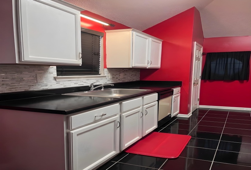 Kitchen featuring dark countertops, white cabinetry, dishwasher, and dark tile patterned floors