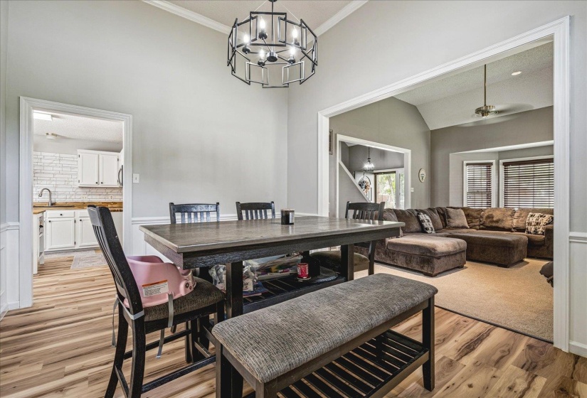 Dining room featuring light wood-style floors, a chandelier, crown molding, a ceiling fan, and a high ceiling