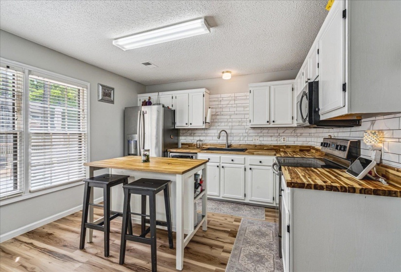 Kitchen featuring butcher block counters, stainless steel appliances, white cabinets, light wood-type flooring, and a textured ceiling