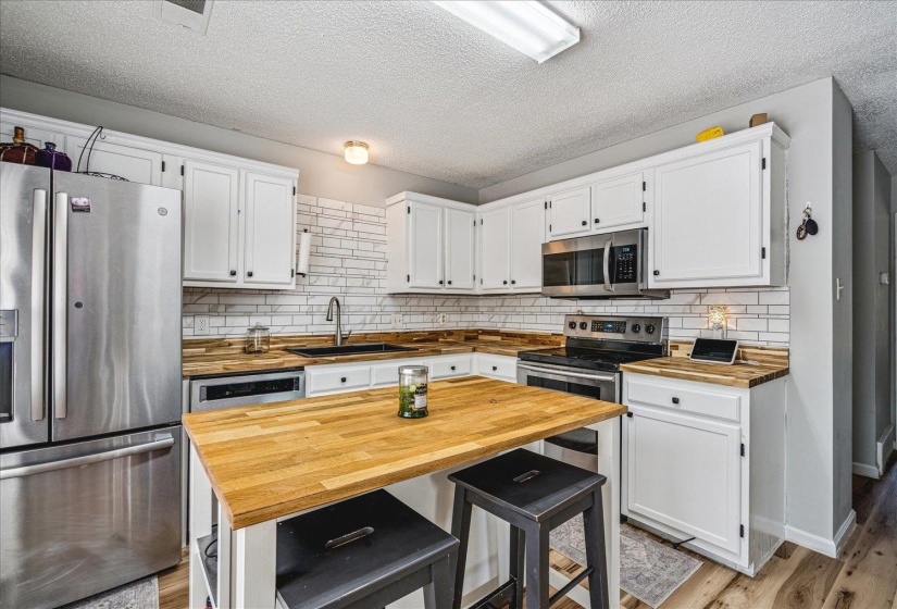 Kitchen with stainless steel appliances, butcher block countertops, white cabinets, light wood-type flooring, and a textured ceiling
