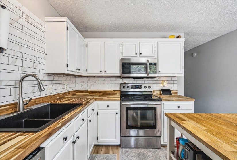 Kitchen with butcher block counters, stainless steel appliances, white cabinetry, light wood-type flooring, and a textured ceiling