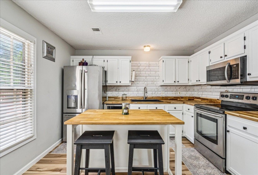 Kitchen featuring wood counters, stainless steel appliances, light wood-type flooring, white cabinetry, and a textured ceiling