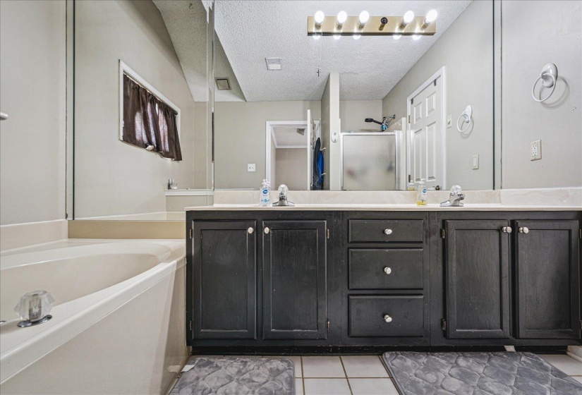 Full bathroom with double vanity, light tile patterned flooring, a textured ceiling, a garden tub, and a stall shower