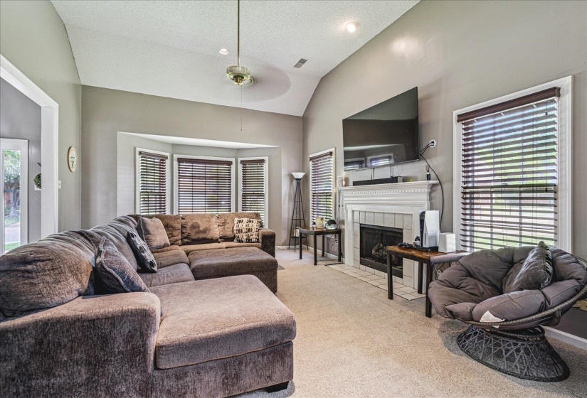 Carpeted living area featuring a high textured ceiling, a tiled fireplace, and ceiling fan
