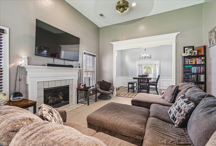 Carpeted living area with a tiled fireplace, wainscoting, hanging lights, a decorative wall, and a ceiling fan
