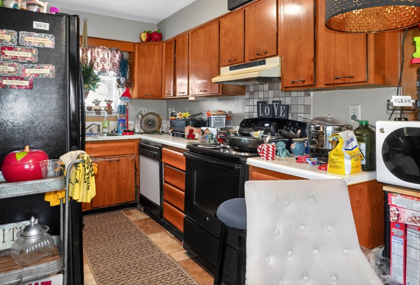 Kitchen featuring black appliances, wood finish cabinetry, light countertops, and decorative backsplash