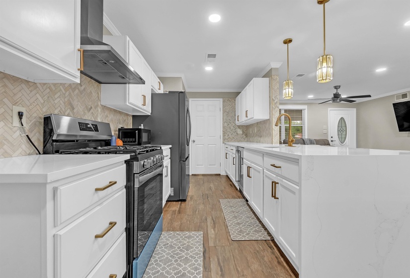 Kitchen featuring a peninsula, stainless steel appliances, white cabinetry, light stone countertops, and ornamental molding