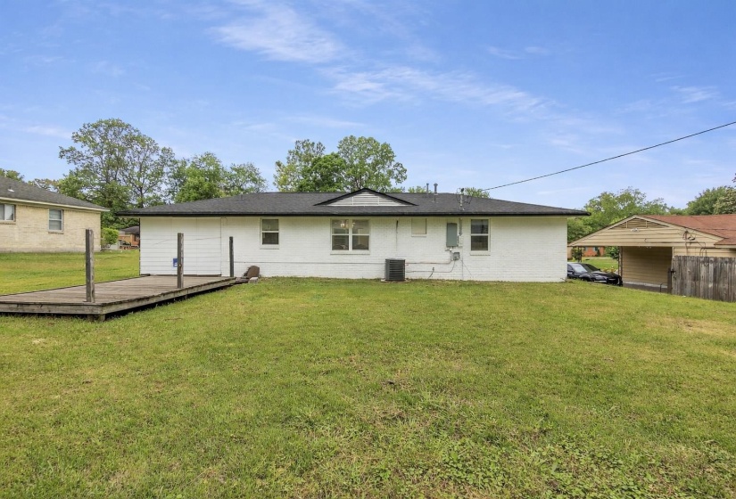 Rear view of house with a wooden deck, a lawn, and brick siding