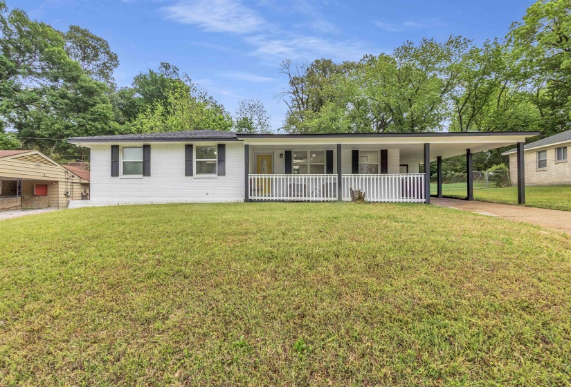 Ranch-style home featuring a front yard, brick siding, driveway, an attached carport, and covered porch