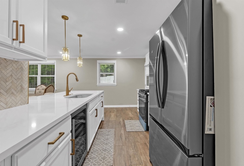 Kitchen with stainless steel appliances, white cabinets, light stone countertops, light wood finished floors, and hanging light fixtures