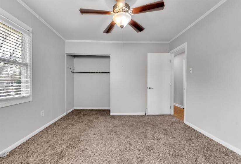 Unfurnished bedroom with a closet, light colored carpet, crown molding, and a ceiling fan