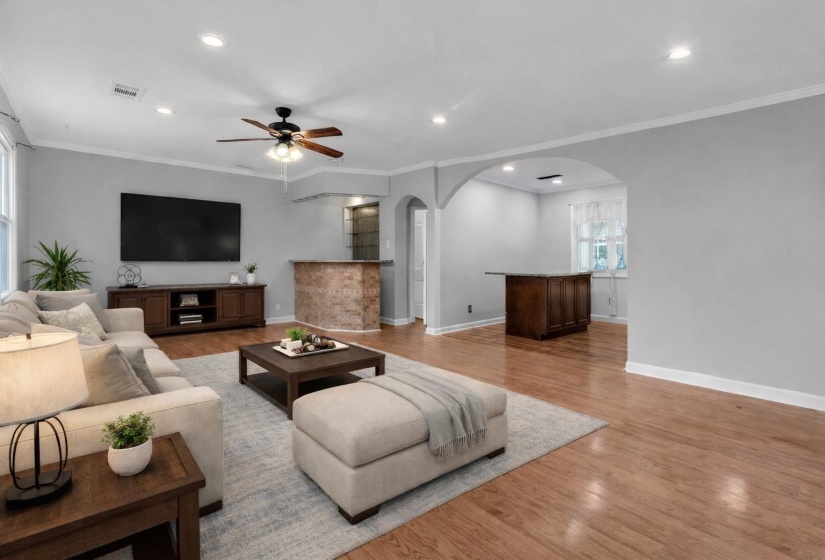 Living room with light wood-style flooring, arched walkways, ornamental molding, a ceiling fan, and recessed lighting