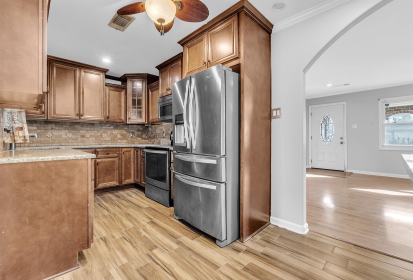 Kitchen featuring arched walkways, stainless steel appliances, a ceiling fan, wood finish floors, and wood finish cabinets