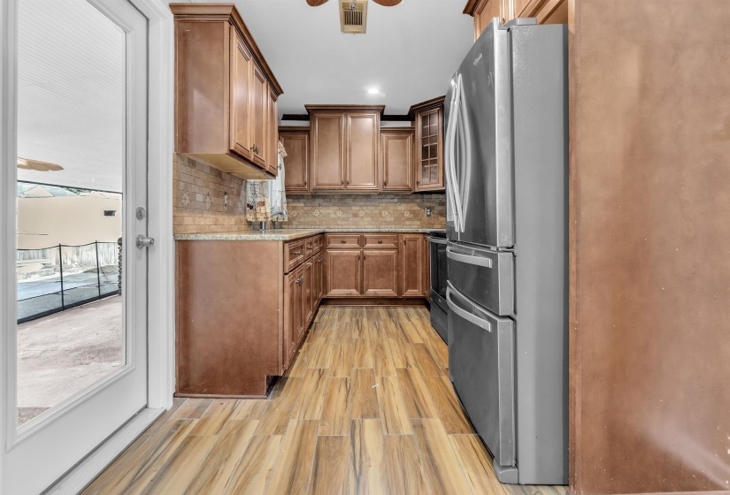 Kitchen featuring stainless steel appliances, wood finish cabinetry, light wood finished floors, ceiling fan, and glass insert cabinets