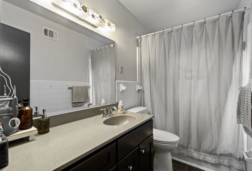 Full bathroom featuring vanity, a shower with shower curtain, tile walls, dark tile patterned floors, and wainscoting
