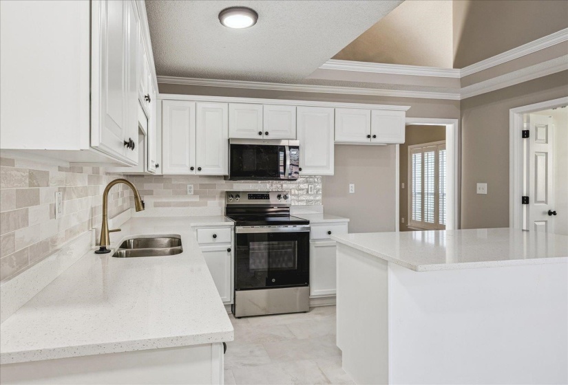 Kitchen with stainless steel appliances, white cabinetry, crown molding, light stone countertops, and a textured ceiling