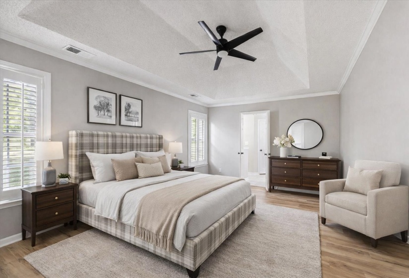 Bedroom featuring a textured ceiling, ornamental molding, light wood-style flooring, a ceiling fan, and a raised ceiling