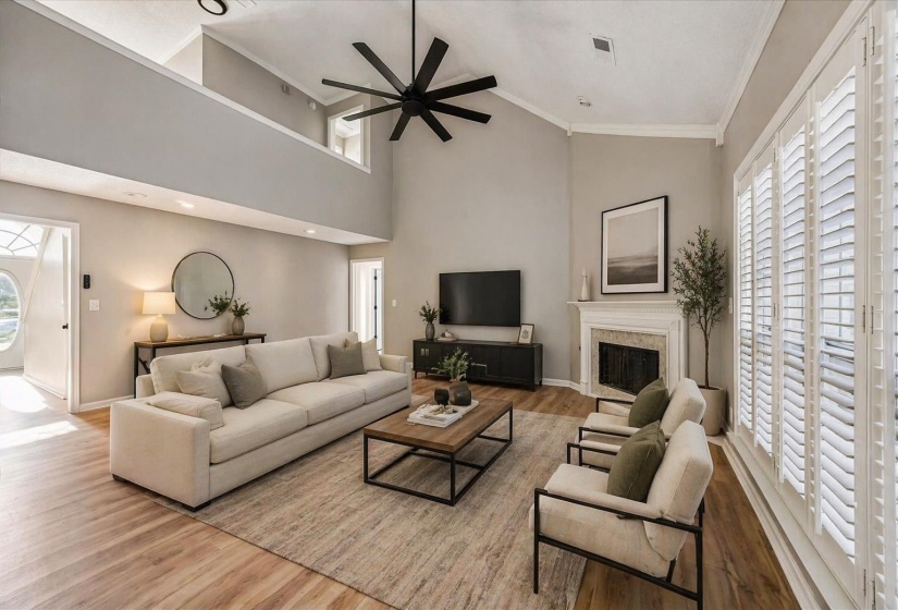 Living area featuring light wood-style floors, ceiling fan, vaulted ceiling, crown molding, and a glass covered fireplace
