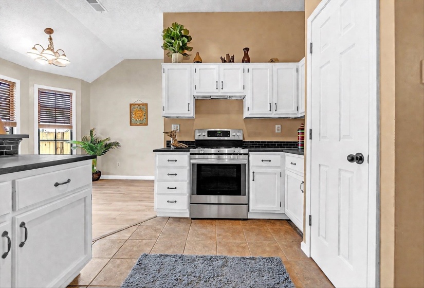 Kitchen with white cabinetry, dark countertops, stainless steel electric range, vaulted ceiling, and light tile patterned flooring