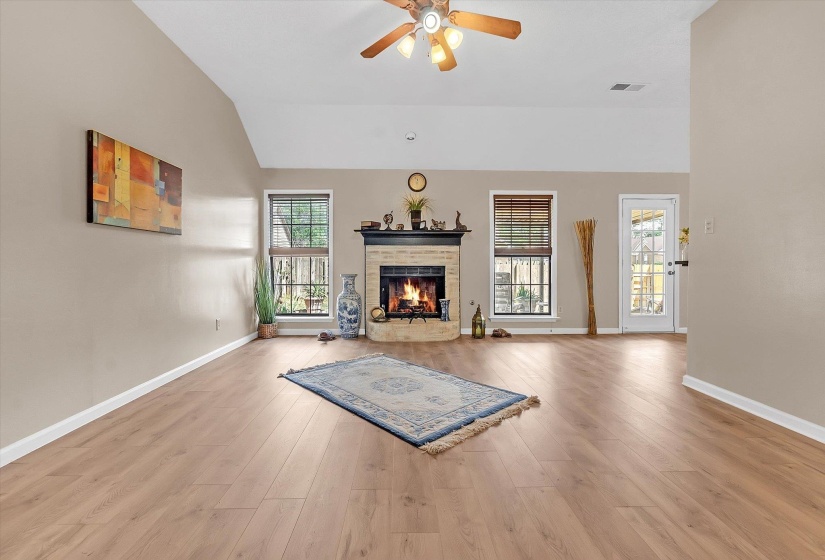 Living area with ceiling fan, lofted ceiling, light wood-style floors, and a warm lit fireplace