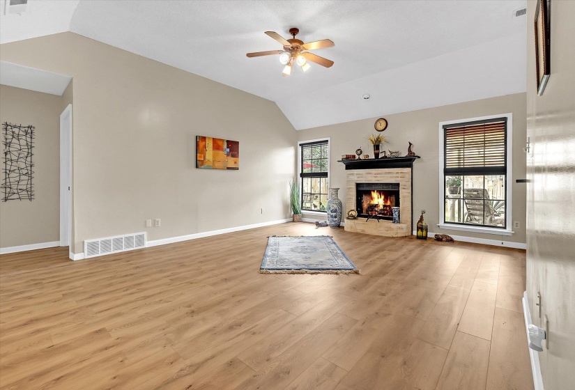 Unfurnished living room featuring lofted ceiling, light wood-style floors, ceiling fan, and a brick fireplace