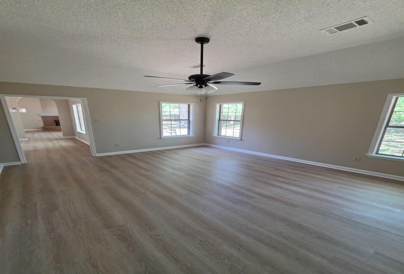 Empty room featuring light wood-type flooring, healthy amount of natural light, a textured ceiling, a ceiling fan, and arched walkways