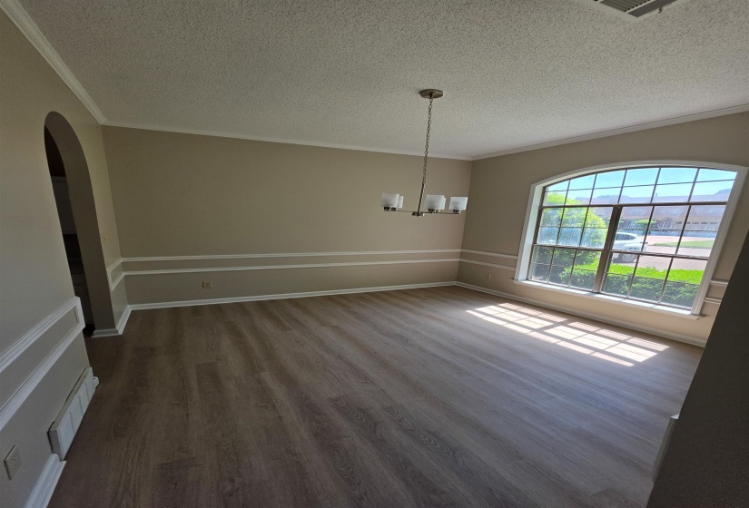 Dining area featuring arched walkways, ornamental molding, a textured ceiling, light wood finished floors, and hanging lights