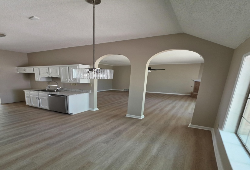 Kitchen featuring white cabinets, light wood-style floors, arched walkways, light countertops, and stainless steel dishwasher, stove and microwave.  New cabinet pulls and lighting.