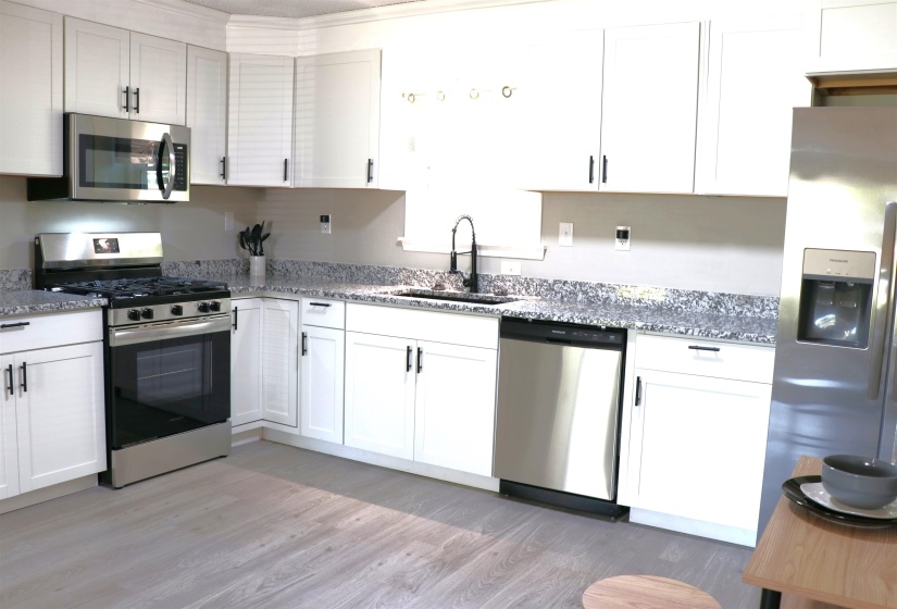 Kitchen featuring stainless steel appliances, white cabinets, and light stone counters