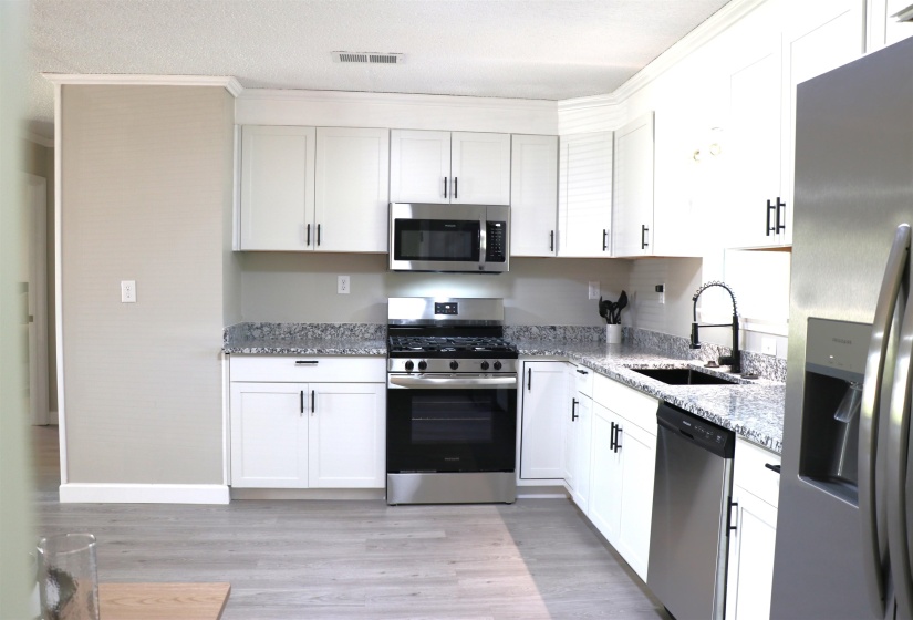 Kitchen with stainless steel appliances, light stone counters, white cabinets, light wood-type flooring, and crown molding