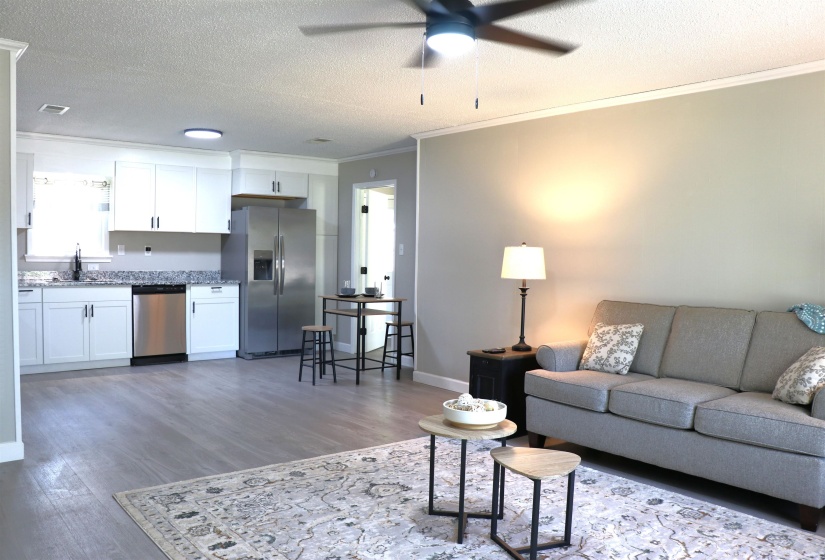 Living area with a textured ceiling, ornamental molding, a ceiling fan, and dark wood-type flooring