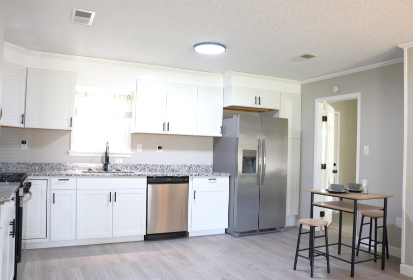 Kitchen featuring stainless steel appliances, white cabinetry, light stone counters, a textured ceiling, and light wood finished floors