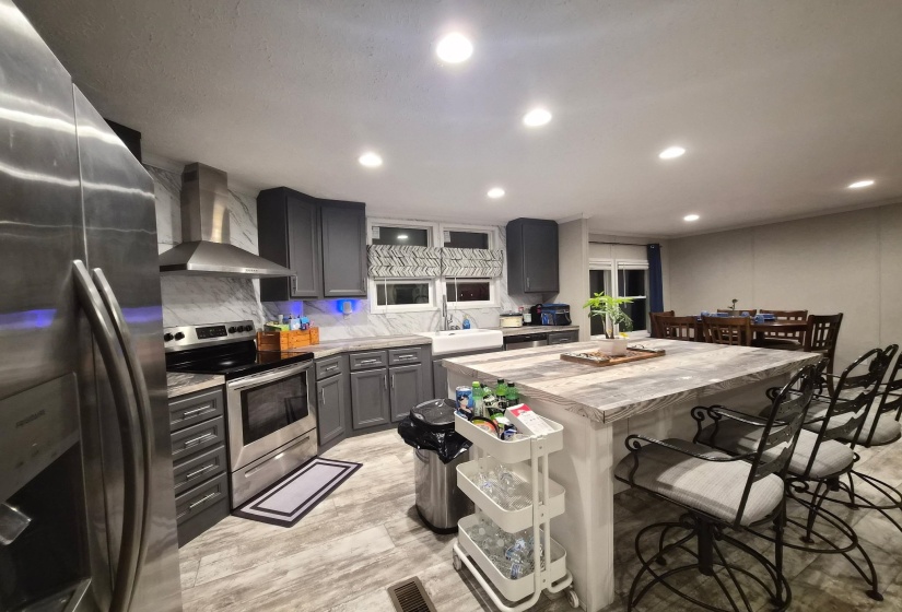 Kitchen with stainless steel appliances, a kitchen breakfast bar, recessed lighting, decorative backsplash, and light wood-type flooring