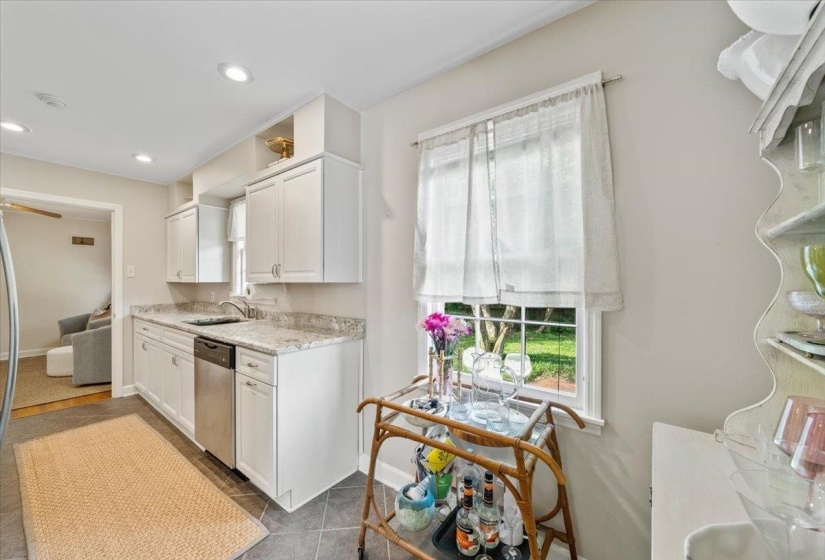 Kitchen featuring white cabinetry, plenty of natural light, dishwasher, and light stone counters