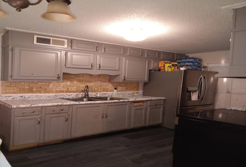 Kitchen featuring a textured ceiling, crown molding, stainless steel fridge, light countertops, and dark wood-style floors