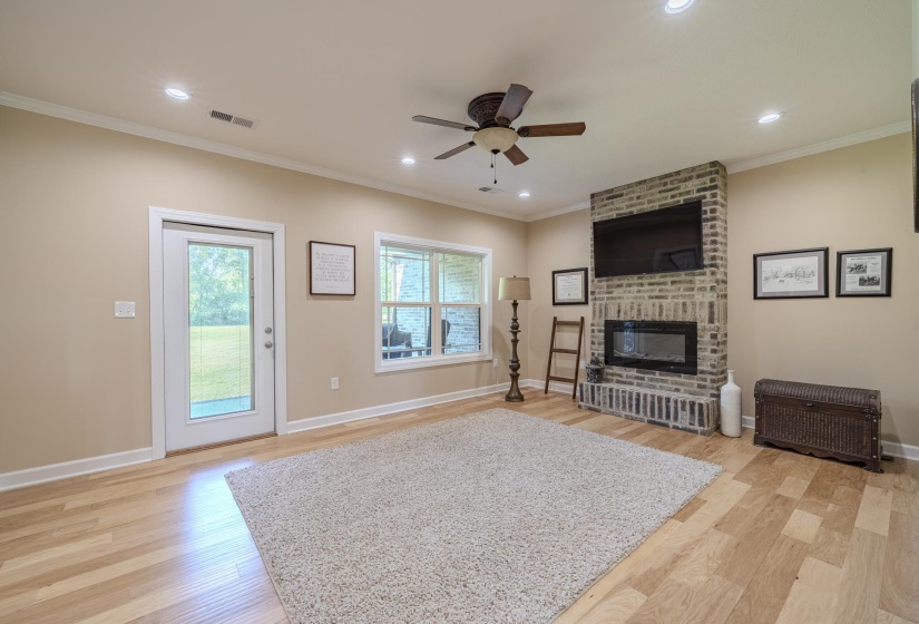 Living area featuring a ceiling fan, light wood-style flooring, a brick fireplace, ornamental molding, and recessed lighting