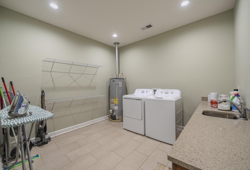Laundry area with gas water heater, washing machine and dryer, recessed lighting, and light tile patterned floors