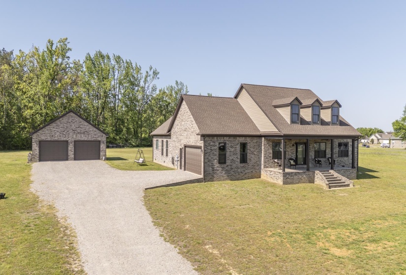 Cape cod house featuring a front yard, a porch, a shingled roof, a detached garage, and brick siding