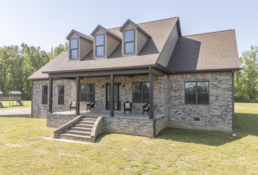 Cape cod house featuring covered porch, a front yard, brick siding, roof with shingles, and a playground