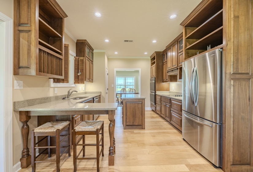 Kitchen with open shelves, a kitchen breakfast bar, stainless steel appliances, light stone counters, and crown molding