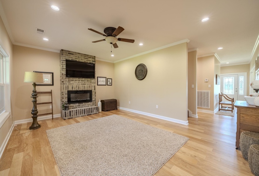 Living room featuring a ceiling fan, light wood finished floors, a brick fireplace, recessed lighting, and ornamental molding
