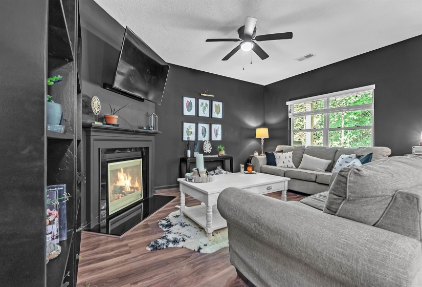 Living room featuring a fireplace with flush hearth, dark wood-style flooring, and ceiling fan